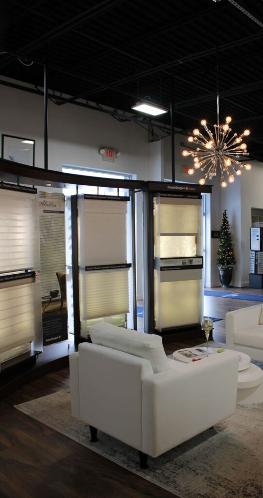 Modern window treatment showroom featuring Hunter Douglas blinds displays, white lounge chairs, hardwood floors, and contemporary chandelier lighting