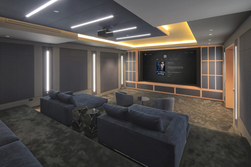 Luxury home theater with recessed lighting, acoustic wall panels, ceiling-mounted projector, and large screen designed for an immersive cinematic experience.