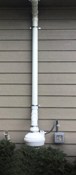 Radon Mitigation System Installed alongside a vinyl-sided tan house