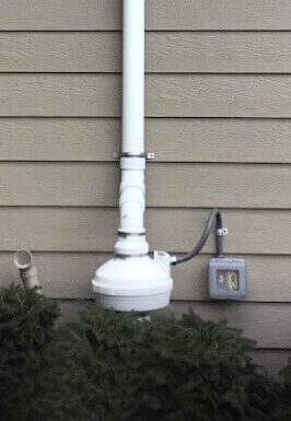 Radon Mitigation System Installed alongside a vinyl-sided tan house